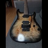 Elektrická kytara s tělem z přírodně vybarveného dřeva s výraznou strukturou a černým přechodem k okrajům. Nástroj má dva černé humbuckery, černý tre…