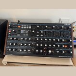 Černý polyfonní syntetizátor Novation Peak v dřevěném šasi. Na displeji je zobrazen text „Himalaya SS 1/1“, „raw“, „Category All“. Přední panel obsah…