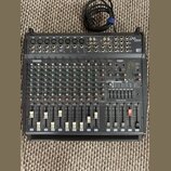 Černý mixovací pult s nápisy YAMAHA a EMX 2000. Zařízení obsahuje početné vstupní kanály s potenciometry, přepínači a posuvníky. V pravé části je umí…