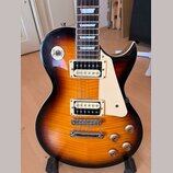 Elektrická kytara s tónem sunburst (oranžová a hnědá) a krémovým plechtrzem. Nástroj má dva humbuckery s bílými rámečky, chromovaný most a stopku. Na…