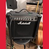 Kytarový kombo zesilovač značky Marshall, model MG15CFX. Má černý povrch s karbonovou texturou a stříbrný ovládací panel s několika otočnými knoflíky…