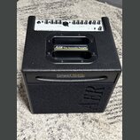 Černý akustický zesilovač s texturovaným povrchem. Na přední straně je nápis „Compact Mobile2 battery-powered acoustic amplifier“ a v dolní části rel…