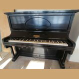 Černý piano (pianino) s otevřenou horní deskou, která obsahuje oválný reliéfní ornament. Nad klávesnicí je umístěno zlaté logo s nápisem "Bechstein".…