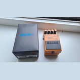 Na fotografii je oranžový kytarový efekt BOSS TURBO Distortion DS-2 v originální černé krabici. Na pedálu jsou viditelné čtyři ovládací knofíky, nápi…