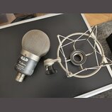 Dynamický mikrofon s kovovou síťkovou hlavou a šedým tělem. Na těle je nápis TRION 7000 DUAL ELEMENT PERSON a logo ve tvaru stylizovaného písmena T.…