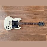 Bílá elektrická kytara s černým plechtrátem a hnědým hmatníkem. Na hlavě kytary je bílý nápis Epiphone a pod ním označení SG. Nástroj vykazuje mírné…