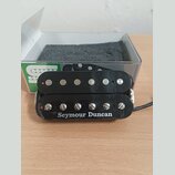 Černý humbucker s dvěma řadami magnetických pólů. Na spodní části je bílý nápis Seymour Duncan. Povrch plastového krytu vykazuje drobné škrábance a z…