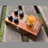 Bronzový kytarový efekt s nápisy MXR, BASS INNOVATIONS a bass fuzz deluxe. Zařízení má čtyři černé plastové knofíky a jeden velký průsvitný oranžový…