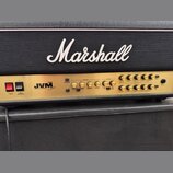 Kytarový zesilovač s zlatým předním panelem umístěný před černou Marshall boxovou skříní s bílým logem Marshall. Na panelu je nápis JVM 200watt a řad…