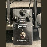 Černý kytarový efekt MXR reverb. Na horní straně jsou tři černé otočné ovnovátka s popisky DECAY, TONE a MIX. Uprostřed se nachází přepínač s nápisy…