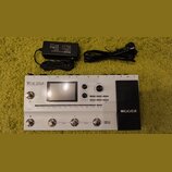 Bílý kytarový procesor s černým pedálem, na kterém je nápis MOOER. Na horní části přístroje je displej a text VCE 250 amp modelling & multi-fx. Vedle…