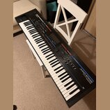 Černý digitální klavír s bílými a černými klávesami. Na horním panelu jsou viditelné nápisy Roland, JUNO-STAGE a SOUND MODIFIER. Přístroj obsahuje ně…