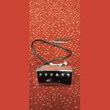 Kromě chromovaného humbuckerového snímače s šesti viditelnými šrouby jsou na červeném podkladu dvě šroubky a jedna pružina. Na bílém kabelu je vidite…