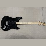 Černá elektrická kytara s jasným dřevěným hmatníkem a černým pickguardem. Na hlavě je viditelné logo Squier a nápis Stratocaster. Nástroj vykazuje zn…