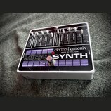 Kytarový efekt v bílém šasi s černým horním panelem. Na panelu je nápis MICROSYNTH a logo electro-harmonix s doplňkem MADE IN NYC, USA. Horní část ob…