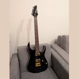 Černá elektrická kytara s tmavým hnedým hmatníkem a zlatým hardwarem. Na hlavě je bílý nápis Ibanez. Kytara má dva humbuckery, dvě otočné potenciomet…