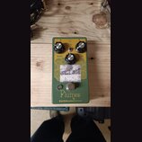 Zelený kytarový efekt s nápisy Plumes a EarthQuakerDevices®. Na horní straně jsou tři černé kontrolní knoflíky s popisky Level, Tone a Gain a přepína…