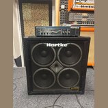 Černý basový reproduktor Hartke s čtyřmi membránami za kovovou mřížkou. V pravém dolním rohu je štítek s nápisem VX series ULTRA PACK a v horní části…