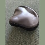 Černý polstrovaný sedák v ergonomickém tvaru. Povrch je z hladkého materiálu s viditelným prošíváním po okraji. Na fotce nejsou žádné viditelné značk…