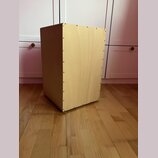 Světle hnědý, dřevěný reproduktorový box s hranatým tvarem. Boční stěna je spojena šrouby viditelnými v řadě podél hran. Povrch dřeva je hladký bez v…
