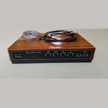 Stereo zesilovač v dřevěném šasi s černým čelním panelem. Na panelu je nápis MODEL AZS 100 L STEREO a logo TESLA. Jsou zde čtyři otočné ovladače, něk…