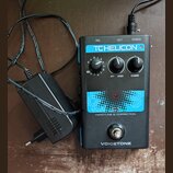 Černý efekt pedál s modrými prvky a nápisy TC HELICON, C1 HARDTUNE & CORRECTION a VOICETONE. Zařízení má tři ovládací knoflíky, jeden spínací pedál a…