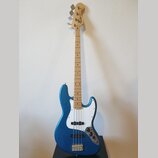 Modrá elektrická basová kytara s bílým pickguardem a světlou hnedou hmatníkem. Na hlavě nástroje je viditelné logo Fender a nápis MADE IN USA. Nástro…
