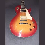 Elektrická kytara s tvarem singlecut a povrchovou úpravou v červeno-žlutém přechodu (sunburst). Nástroj má dva humbuckery, bílý plechtrum a čtyři zla…