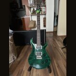 Zelená elektrická kytara s výraznou strukturou dřeva na těle a hnedým hmatníkem. Na hlavě je viditelné logo PRS. Kytara má dva humbuckery, fixační mo…