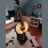 Na fotografii je hybridní nástroj kombinující kontrabas a buben. Na bílém bubnovém povrchu je černý nápis „Country music session Kontrabass Banjo“. N…