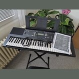 Černý digitální klavír značky YAMAHA, model YPT-340. Nástroj je umístěn na černém skládacím stojanu a je vybaven přiloženým napájecím kabelem a uživa…