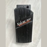 Černý volume pedál s žebrovaným povrchem. Na horní části je bílý nápis VOLUME a červený nápis MONO, pod kterými jsou dvě červené vlnovky. V horní čás…