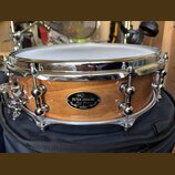 Dřevěný buben s přirozeným povrchem a chromovanými obručemi. Na korpusu je oválný černý štítek s nápisy „PETER ERSKINE“, „Jazz Snare“ a logem „TAMA“.…