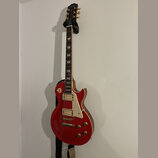 Červená elektrická kytara typu Les Paul s bílým pickguardem a dvěma humbuckery. Na hlavě je zlatý nápis „Les Paul“ a podpis „Jimmy Page“. Kytara má z…