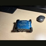 Modrá DI box s černými gumovými nárazníky na rozích. Na horní straně je bílý nápis SAMSON a schéma zapojení s texty INPUT, PAD, HIGH Z, BATTERY PHANT…