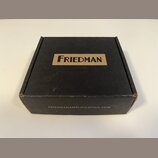 Černá papírová krabička s hnědým obdélníkovým polem, ve kterém je černý nápis FRIEDMAN. Na spodní hraně krabice je uveden web FRIEDMANAMPLIFICATION.C…