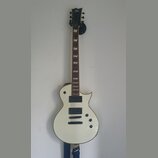 Bílá elektrická kytara s černým hmatníkem a dvěma humbuckery. Na hlavě je bílé logo ltd. Tělo má dva ovládací knofíky a kytara visí na nástěnním držá…
