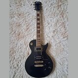 Černá elektrická kytara s tvarem single-cutaway a hnědým hmatníkem. Na hlavě je bílý nápis Lizmaud. Kytara má dva humbuckery, čtyři ovládací knoflíky…
