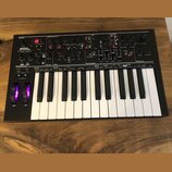 Černý syntetizátor s klaviaturaí a ovládacími prvky v horní části. Na levé straně je nápis NOVATION AFTERTOUCH XL. Přístroj obsahuje početné otočné k…