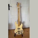 Světle béžová elektrická basová kytara s přírodním dřevěným hnedem krku a hmatníkem. Na hlavě je viditelné logo "Squier". Tělo nástroje má dva snímač…