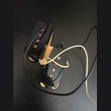 Dvě elektrické kytarové snímače typu humbucker s černými plastovými kryty a viditelnými polkovými magnety. Snímače jsou umístěny na světlém dřevěném…