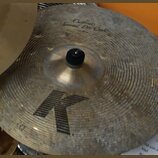Zlatý cimbál s koncentrickými rýhami na povrchu. V horní části je nápis „Custom Special Dir Crash“, ve spodní části je velké černé písmeno „K“. Povrc…