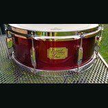 Tmavě červený buben s kovovými obručmi a napínacími šrouby. Uprostřed korpusu je zlatý nápis Export Series DRUMS Pearl. Povrch nástroje je lesklý a v…