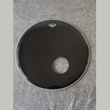 Černá bubnová blána s vyříznutým otvorem v dolní části. V horní části je bílé logo REMO a pod ním menší nečitelný nápis. Povrch je hladký a lesklý be…
