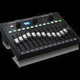 Černý mixovací pult značky behringer, model P24. Zařízení obsahuje 12 posuvníků s bílými knoflíky, řadu zelených tlačítek s čísly 1 až 12 a modrý dis…