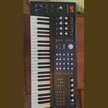 Černý syntetizátor s klaviaturaí. Na horním panelu je oranžové logo ASM Electric Music Company a nápis HYDRASYNTH. Přístroj obsahuje numeroustovací k…