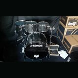Černá bicí souprava značky SONOR, model SQ2. Sestava obsahuje basový buben s nápisem SONOR a SQ2, dva tom-tomy a jeden floor tom. Vedle nástrojů jsou…