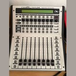 Stříbrný digitální mixovací kontroler s nápisem motor mix Digital Mixer Worksurface a logem cm. Zařízení obsahuje LCD displej, řadu otočných knoflíků…