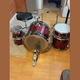 Červená bicí souprava s kovovými obručmi, zahrnující basový buben, tom a snare. Na sedáku je viditelné logo MAPEX a na pedálu nápisy IRON COBRA 500 a…