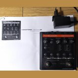 Černý efektový pedál s oranžovým pruhem, na kterém je nápis TC-HELICON harmonyM a VOICETONE™. Zařízení obsahuje několik otočných potenciometrů, tlačí…